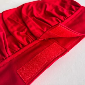 May include: Red chef's hat with a velcro fastening. The hat is made from a soft, stretchy fabric.