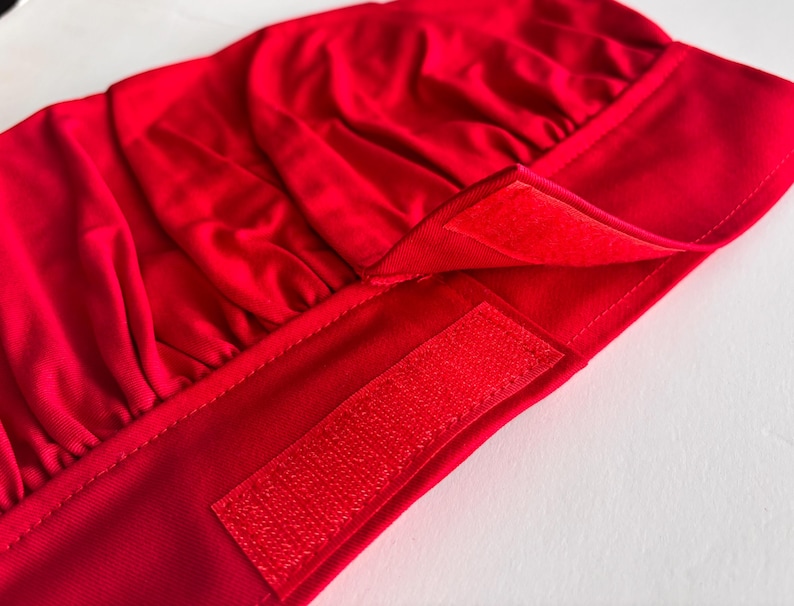 May include: Red chef's hat with a velcro fastening. The hat is made from a soft, stretchy fabric.