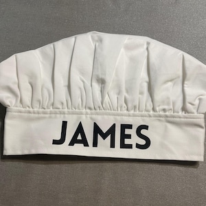 May include: White chef's hat with the name "JAMES" printed in black on the front.