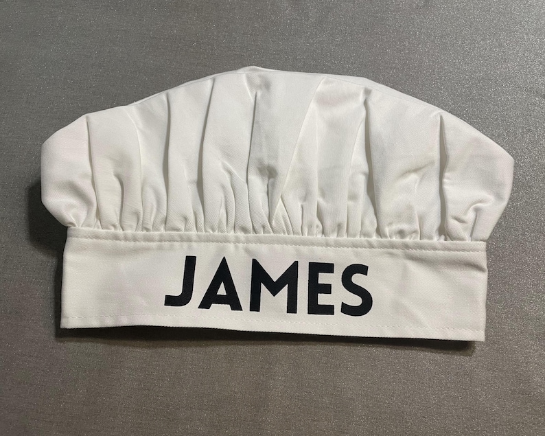 May include: White chef's hat with the name "JAMES" printed in black on the front.