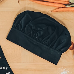 May include: A black chef's hat with a pleated design. The hat is made of a soft, fabric material.