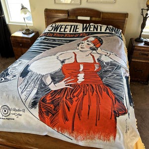 Può includere: Una coperta in stile vintage con un'illustrazione in bianco e nero di una donna con un vestito rosso. La coperta presenta il testo "SWEETIE WENT AWAY" e "Say Where-When-or Why". Lo sfondo è color crema.