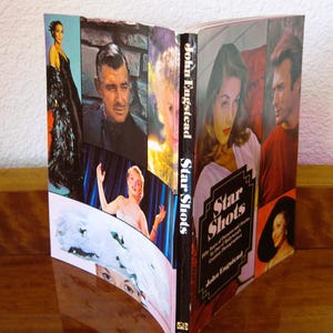 May include: An open book titled "Star Shots" featuring a collage of vintage Hollywood portraits. The cover displays the title in a stylized font, with the author's name, John Engstead, below. The book is on a wooden surface.