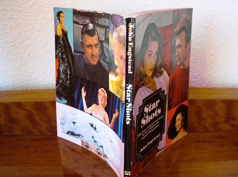 May include: An open book titled "Star Shots" featuring a collage of vintage Hollywood portraits. The cover displays the title in a stylized font, with the author's name, John Engstead, below. The book is on a wooden surface.