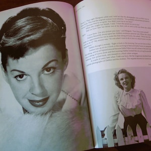 May include: A black and white photograph of a woman with dark hair and red lipstick, featured in a book. The image is a close-up of the woman's face, with a soft focus. The book is open, with text and another photograph visible.