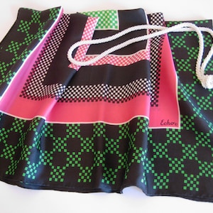 May include: A black silk scarf with a green and pink geometric pattern. The scarf has a white tassel and the word "Echo" is printed on the scarf.