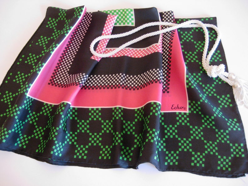 K&ouml;nnte beinhalten: Ein schwarzer Seidenschal mit einem geometrischen Muster in Gr&uuml;n und Rosa. Der Schal hat einen wei&szlig;en Quasten und das Wort "Echo" ist auf den Schal gedruckt.