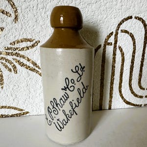 May include: A vintage stoneware bottle with a brown top and a cream-colored body. The bottle has black script that reads "E.P. Shaw & Co. Ltd. Wakefield". The bottle is likely an antique.