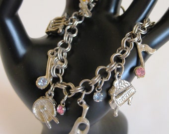 May include: A silver charm bracelet with musical instrument charms, including a piano, a drum, a trumpet, and a music note. The bracelet has a silver chain and is adorned with small, colorful rhinestones.
