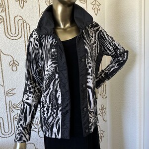 May include: A black and white jacket featuring a bold animal print pattern, a solid black high collar, and a vertical black button placket. The jacket has long sleeves and is worn over a plain black top, showcasing a contrasting design.