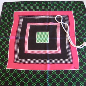 K&ouml;nnte beinhalten: Ein schwarzer Seidenschal mit einem geometrischen Muster aus gr&uuml;nen, wei&szlig;en und rosa Quadraten. Der Schal hat einen wei&szlig;en Quasten und das Wort "Echo" ist in der rechten unteren Ecke aufgedruckt.