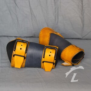 May include: Two leather wrist cuffs with adjustable buckles. One cuff is dark blue with yellow straps and the other is yellow with dark blue accents.