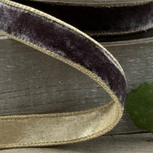 May include: A roll of dark gray velvet ribbon with a gold metallic edge. The ribbon is on a wooden surface.