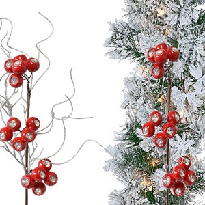 May include: A red berry spray with silver glitter branches and clear rhinestone accents. The spray is shown against a white background and a snowy evergreen tree.