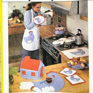 May include: A vintage Simplicity pattern package showing a woman in a kitchen, with a set of 10 kitchen accessories. The accessories include an apron, oven gloves, pot holders, and a house-shaped item, all with a blue chicken design.