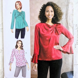 May include: Butterick B6712 sewing pattern featuring three blouse designs. The pattern includes illustrations of a teal long-sleeve blouse, a red long-sleeve blouse with bell sleeves, and a floral print blouse. The pattern's text includes "FABRICLAND".
