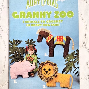 May include: A vintage book cover titled "Aunt Lydia's Granny Zoo" featuring crochet animal patterns. The cover displays a pink pig, a yellow lion, and a brown horse with a colorful blanket. The text reads "7 Animals to Crochet in Heavy Rug Yarn."