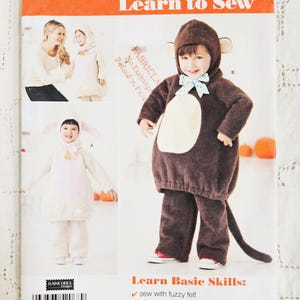 Peut inclure: Une pochette de patron de couture Simplicity 2068 pour costumes d'enfants. La couverture présente des illustrations d'un costume de singe marron avec capuche et d'un costume d'agneau crème avec de longues oreilles. Texte : Learn to Sew et Learn Basic Skills.