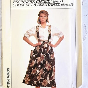 May include: A Simplicity sewing pattern for a skirt with suspenders. The pattern is for a beginner and is level 3. The model is wearing a white shirt and a brown and white floral skirt with suspenders. The pattern is for size 10, EUR 38.