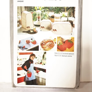 May include: Simplicity pattern 9255. The image shows a sewing pattern with illustrations of kitchen accessories, including a toaster cover, placemat, and apron, all featuring a strawberry design. The pattern is for one size.