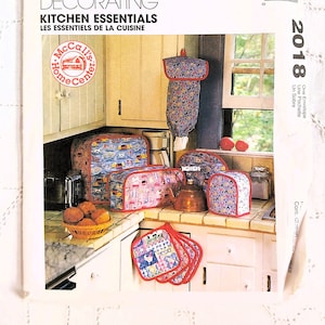 May include: A set of kitchen essentials featuring a red, white, and blue color scheme. The set includes a toaster cover, a microwave cover, a bread basket, a pot holder, and a tea cozy. The items are decorated with a whimsical country-style pattern.