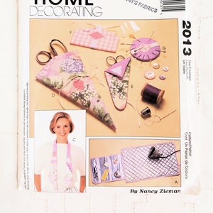May include: A McCall's Home Decorating sewing pattern envelope featuring various sewing tools and accessories. The image includes scissors, pin cushions, spools of thread, and buttons. The pattern is labeled "2013" and includes the text "Fanny's Fabrics."