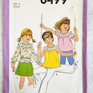 May include: Vintage Simplicity sewing pattern 8499 for children's clothing. The illustration shows three children in various outfits: a floral top and green skirt, a yellow top and white trousers, and a pink top and blue trousers. The pattern is size 6.