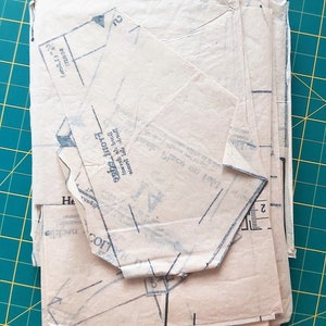 May include: A stack of beige sewing patterns with black lines and text. The top pattern has the text "Front edge" and "Back of garment" printed on it.