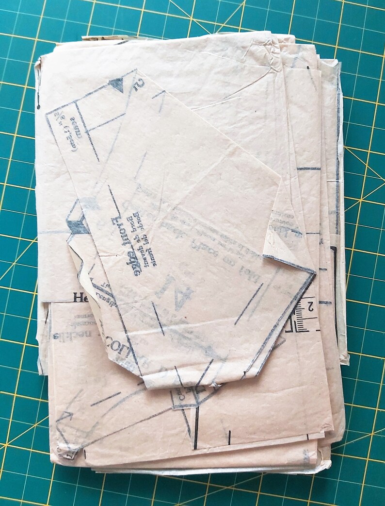 May include: A stack of beige sewing patterns with black lines and text. The top pattern has the text "Front edge" and "Back of garment" printed on it.