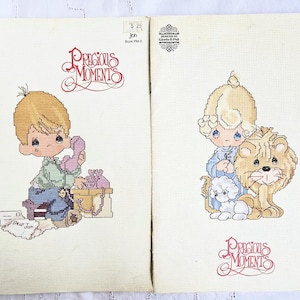 May include: Two cross-stitch patterns featuring Precious Moments characters. The first pattern shows a boy on the phone with the text "Dear Jan" on a piece of paper. The second pattern shows a boy with a lion. The text "Precious Moments" is at the bottom of each pattern.