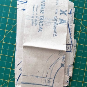 May include: A stack of folded brown paper sewing patterns with blue printed instructions. The pattern is for a jacket sleeve and includes the text "Jacket Sleeve" and "Gimbeldea".