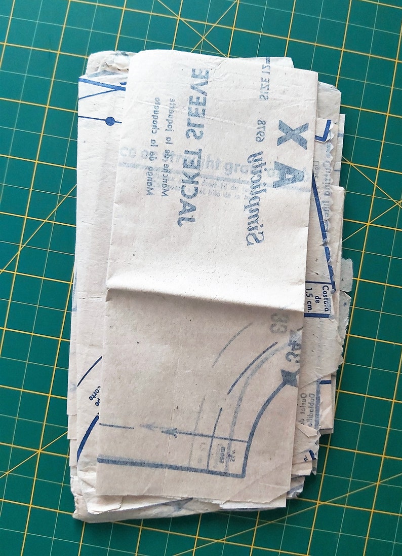 May include: A stack of folded brown paper sewing patterns with blue printed instructions. The pattern is for a jacket sleeve and includes the text "Jacket Sleeve" and "Gimbeldea".
