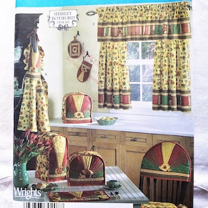 May include: A sewing pattern for a kitchen set, featuring a yellow and brown floral print. The set includes a valance, curtains, a toaster cover, an apron, and chair covers. The pattern is from Simplicity and is designed by Shirley Botsford.