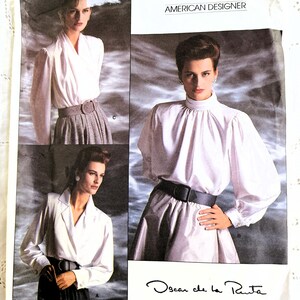 May include: Vogue Patterns American Designer sewing pattern with three blouse designs. The pattern includes a high-collared blouse, a wrap-style blouse, and a collared blouse. The Oscar de la Renta pattern is labelled 1913.
