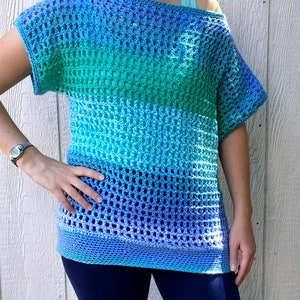 May include: A crocheted top with a blue, green, and purple ombre design. The top has a loose fit and short sleeves.