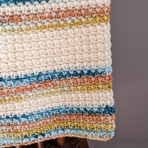 May include: A white crocheted blanket with stripes of blue, teal, yellow, and orange yarn.