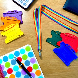 May include: A rainbow lanyard with a silver clip, a notebook with colorful polka dots, a black pen, and several colorful plastic ID card holders.