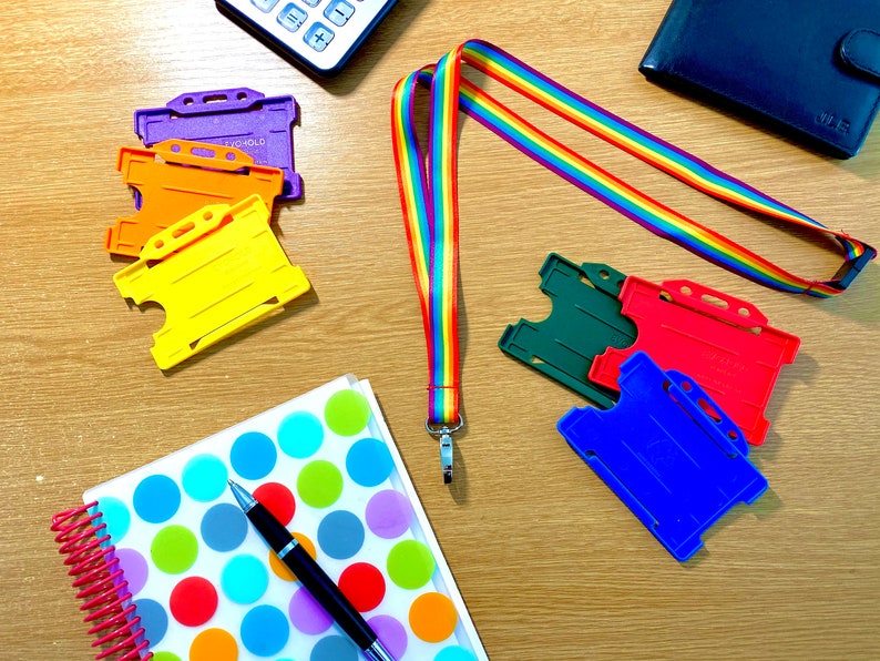May include: A rainbow lanyard with a silver clip, a notebook with colorful polka dots, a black pen, and several colorful plastic ID card holders.