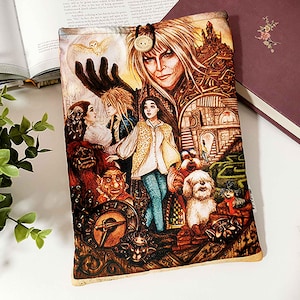 May include: A colorful book cover featuring characters and scenes from the movie Labyrinth. The cover has a button closure and is made of fabric. The artwork includes a clock, a maze, and various fantasy figures.