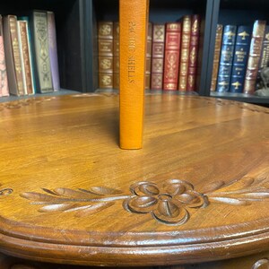 May include: A brown leather-bound book with gold lettering on the spine that reads "Pacific Shells". The book is standing upright on a wooden table with intricate carvings.