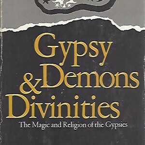 May include: A book cover with a black background and gold text that reads "Gypsy & Demons Divinities: The Magic and Religion of the Gypsies" by Elwood B. Trigg. The top of the cover features a gray illustration of a crescent moon, stars, and a sun with a cross inside.