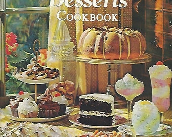 May include: A vintage cookbook titled "Kitchen Fare Desserts Cookbook" with a photo of a table setting with various desserts, including a chocolate cake, cupcakes, a pie, and a bundt cake.
