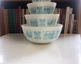 May include: A set of four white ceramic bowls with a blue and white pattern of people, birds, and hot air balloons. The bowls are stacked on top of each other, with the largest bowl on the bottom and the smallest bowl on top.