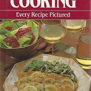 May include: A red and white cookbook cover with the title "ITALIAN COOKING" and the subtitle "Every Recipe Pictured". The cover features a photo of a plate of breaded fish with lemon slices and a side of green pasta.