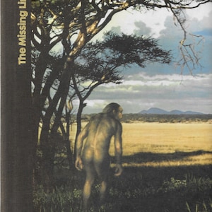 May include: A book cover with the title "The Missing Link" in gold lettering on a black background. The cover features a photo of a hairy, human-like figure standing in a grassy field, looking out at a distant mountain range.