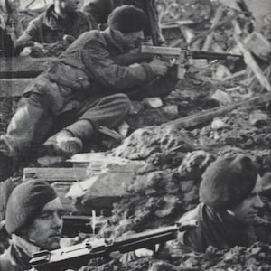 May include: Black and white photograph of soldiers in combat. Several soldiers are crouched or kneeling, aiming rifles. They are wearing dark uniforms and berets, amidst rubble and debris. The image captures a moment of wartime action.