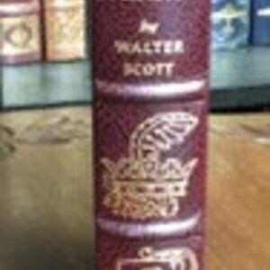 May include: A burgundy leather-bound book with gold accents and the title "Ivanhoe by Walter Scott" on the spine. The book features decorative gold illustrations on the front and back covers.