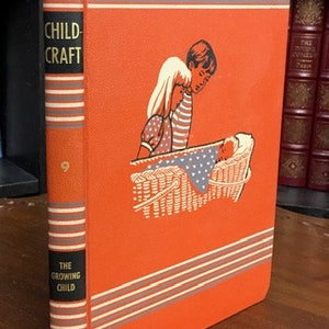May include: Vintage book titled "Child Craft, The Growing Child, Volume 9." The cover is orange with white and gray stripes and an illustration of two children looking at a baby in a basket. The spine is orange with black text.