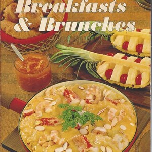 May include: A vintage cookbook titled "Sunset Breakfasts & Brunches" with a photo of a creamy shrimp and seafood dish with almonds, a bowl of orange marmalade, and pineapple slices with cherries on top.