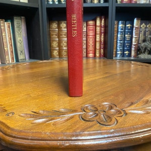 May include: A red leather-bound book with gold lettering that reads "BEETLES" on the spine. The book is standing upright on a wooden table with intricate carvings.